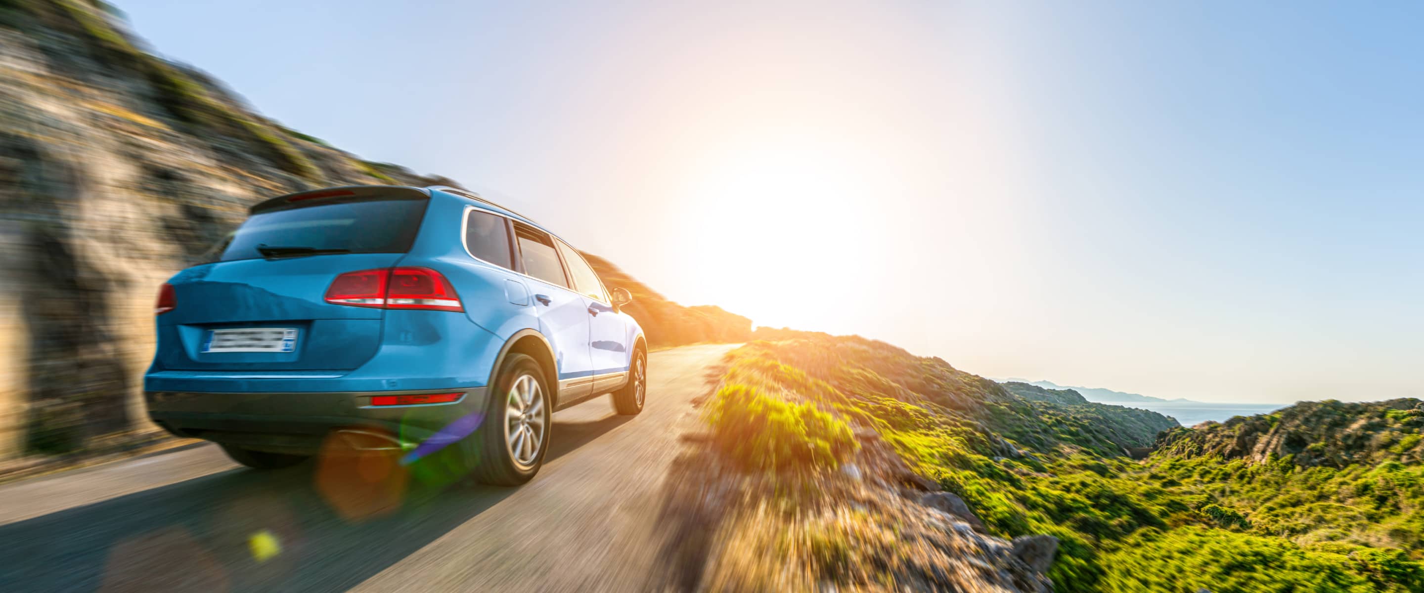 夕日を背景に海岸沿いの道路を走行する青いSUV車
