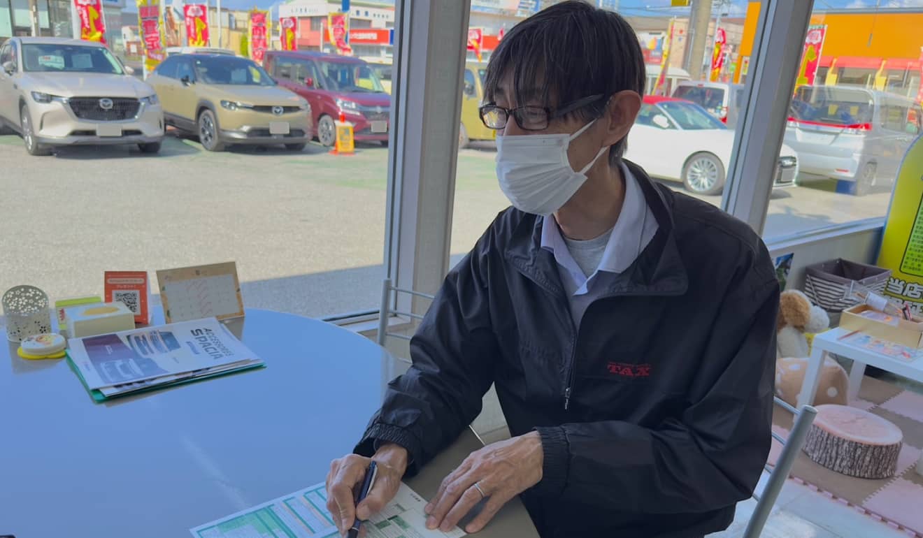 窓越しに展示車両が見える店内で手続きを進めるスタッフ