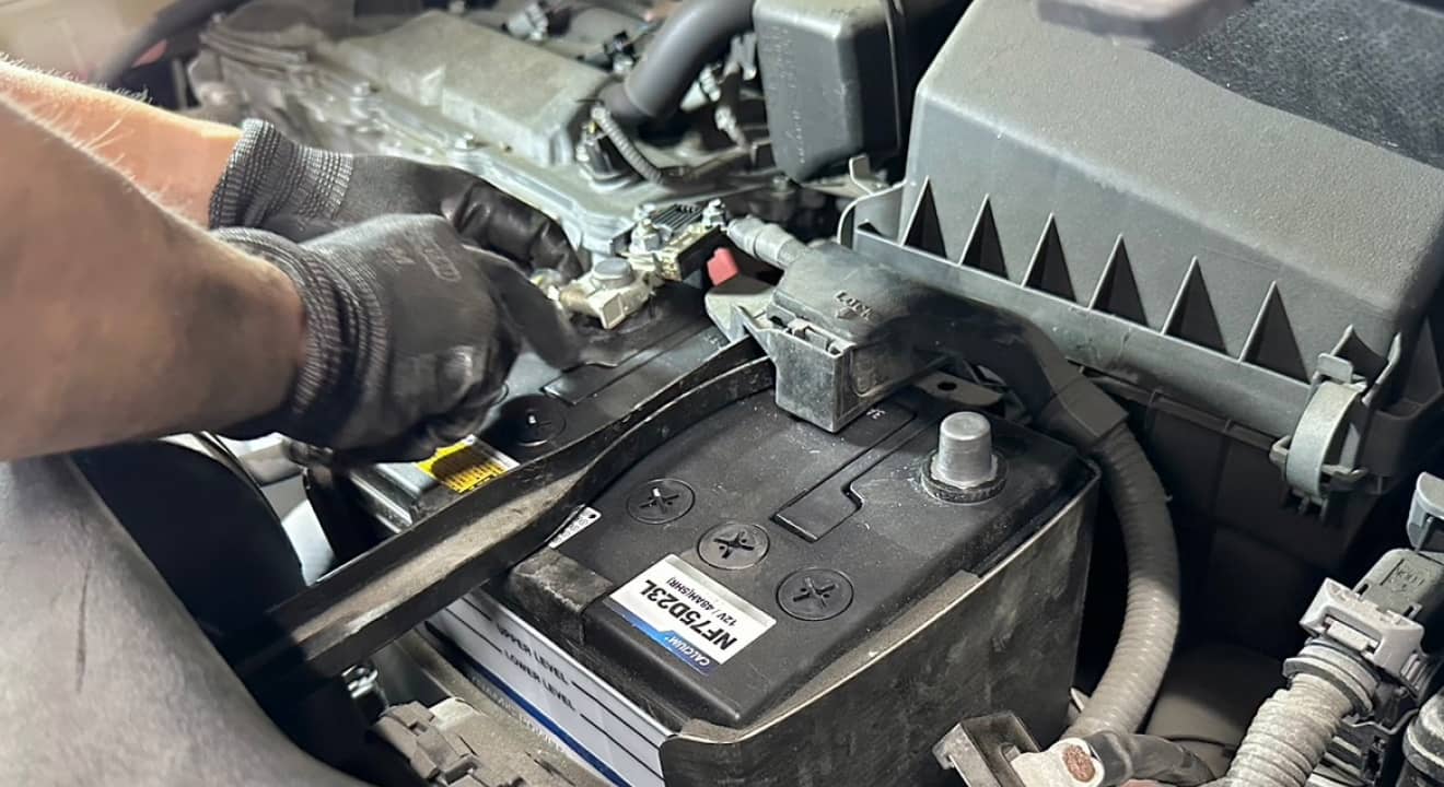 エンジンルーム内でバッテリー端子を調整する整備士