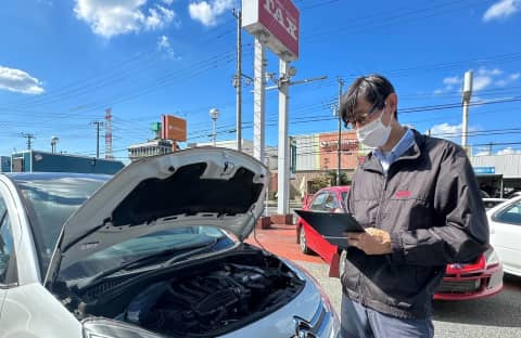 青空の下、車の前で点検リストを確認する男性